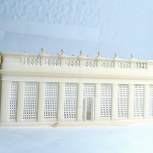 May include: A white, detailed model of a classical building with a balcony and a latticework facade. The model is made of plastic and is approximately 6 inches long.