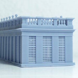 May include: A light gray 3D printed model of a building with a detailed facade and a balcony with a railing. The building has a series of windows with a grid pattern.