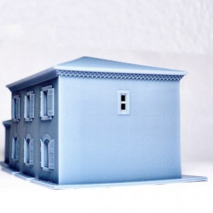 Pu&ograve; includere: Un modello 3D stampato in grigio chiaro di una piccola casa con un design semplice. La casa ha un tetto piatto, alcune finestre e una piccola porta. Il modello &egrave; realizzato in un materiale liscio e opaco.
