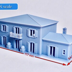 Pu&ograve; includere: Un modello di casa a due piani in scala N, di colore azzurro chiaro, con un balcone bianco, un camino e un tetto in tegole. Il modello misura 12,7 cm di altezza, 11,7 cm di larghezza e 5,4 cm di profondit&agrave;.