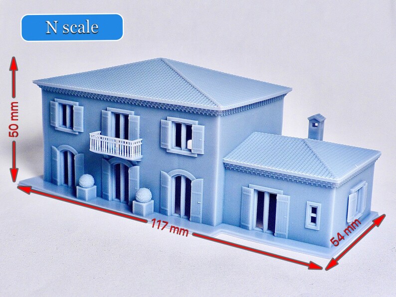 Pu&ograve; includere: Un modello di casa a due piani in scala N, di colore azzurro chiaro, con un balcone bianco, un camino e un tetto in tegole. Il modello misura 12,7 cm di altezza, 11,7 cm di larghezza e 5,4 cm di profondit&agrave;.