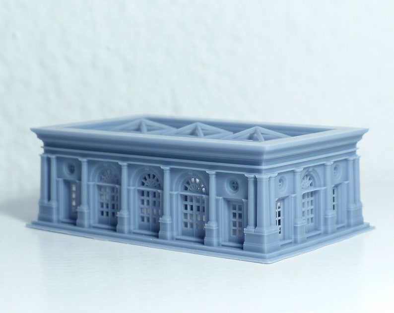 K&ouml;nnte beinhalten: Ein graues 3D-gedrucktes Modell eines Geb&auml;udes mit rechteckigem Sockel und flachem Dach. Das Geb&auml;ude hat eine Reihe von Bogenfenstern und S&auml;ulen.