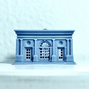 K&ouml;nnte beinhalten: Ein kleines, graues, 3D-gedrucktes Modell eines Geb&auml;udes im klassischen Stil. Das Geb&auml;ude hat einen zentralen Bogen mit zwei kleineren T&uuml;ren auf beiden Seiten. Das Geb&auml;ude hat ein Flachdach und ein dekoratives Gesims.