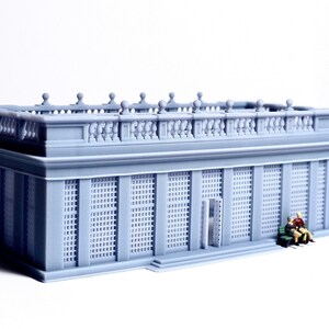 May include: A gray 3D printed model of a building with a balcony and a grid pattern on the windows. Two small figures are sitting on a bench in front of the building.