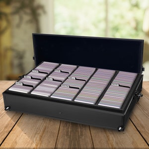 May include: A black storage case with an open lid, filled with multiple stacks of colorful cards. The cards are organized into labeled sections, including "90's Pack," "2013 Holiday Pack," and "Science Pack." The case sits on a wooden surface.