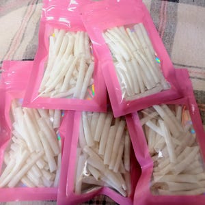 May include: Five individual pink resealable pouches, each containing a collection of small, white, cylindrical, hollow tube-like items. The pouches feature a clear rectangular window on the front, allowing for a view of the white contents inside.