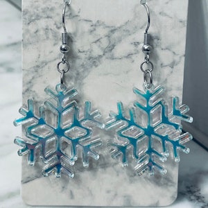 May include: A pair of silver snowflake earrings with a blue iridescent finish. The snowflakes are detailed and intricate.