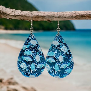 May include: A pair of teardrop-shaped earrings with a blue and white sea turtle pattern. The earrings are made of resin and have silver hooks.