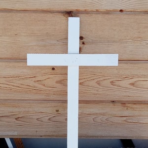 May include: A white wooden cross stake, approximately 24 inches tall, with a pointed end for easy insertion into the ground. The cross is made of simple, unpainted wood.