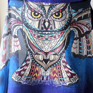 May include: A blue shawl with a large, colorful owl design. The owl is depicted with intricate geometric patterns in shades of gray, beige, teal, and red. The background is a dark blue with a starry pattern, and the shawl has a solid blue border.