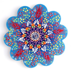 May include: A blue ceramic trivet with a colorful floral design. The trivet is shaped like a flower with 10 petals. The design features red, orange, yellow, green, blue, purple, and white colors.