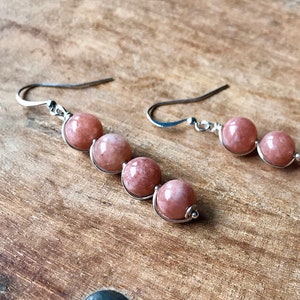 May include: A pair of silver earrings with pink sunstone beads. The beads are strung on wire and dangle from the earrings.