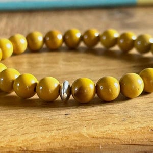 Op de afbeelding: Close-up van een armband met ronde, gele kralen. De kralen worden gescheiden door een zilverkleurige spacer kraal. De gladde kralen zijn in een cirkel gerangschikt. De armband ligt op een houten oppervlak.