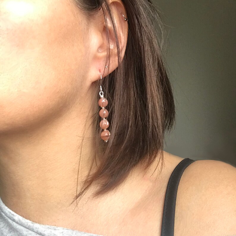 May include: A pair of dangle earrings with a silver chain and multiple brown gemstone beads.