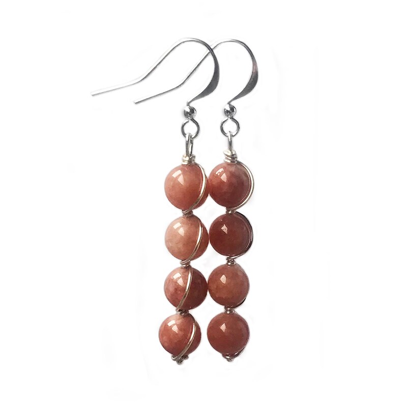 May include: A pair of silver dangle earrings with five peach-colored gemstone beads on each earring. The beads are wrapped in silver wire.