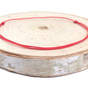 Op de afbeelding: Een rood koord armbandje op een houten oppervlak. Het koord is in een eenvoudige knoop geknoopt.