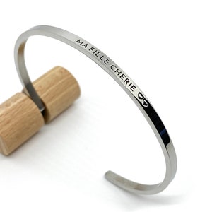 Peut inclure: Un bracelet jonc argenté avec l'inscription "MA FILLE CHERIE" et un symbole de cœur.