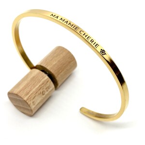 Peut inclure: Bracelet jonc en or avec l'inscription "MA MAMIE CHERIE" et un petit symbole de fleur.
