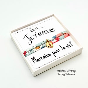 Peut inclure: Une boîte blanche avec un ruban à motif floral et un charme doré. La boîte contient une carte avec le texte "Et si... Je t'appelais Marraine pour la vie?" et le texte "Cordon Liberty Betsy Petunia".