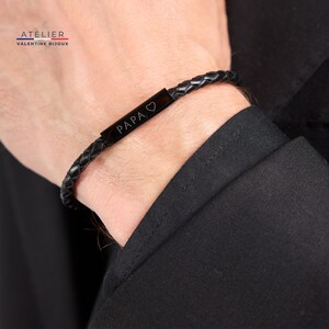 May include: Black leather bracelet with a black metal plate engraved with the word "PAPA" and a heart symbol.