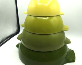 May include: A stack of four nesting bowls in shades of green and yellow. The bowls are arranged from largest to smallest, with the largest bowl at the bottom in a dark green color. The top bowl is yellow.