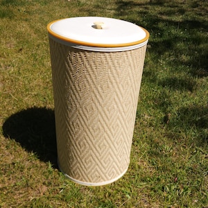 May include: A cylindrical laundry hamper featuring a woven beige exterior with a repeating diamond pattern. The hamper includes a solid white circular lid with a small central knob and a thin orange trim around the edge of the lid.