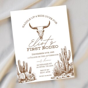Könnte beinhalten: Eine weiße Einladungskarte mit braunem Text und Illustrationen. Der Text lautet "Saddle Up & Ride Over For" über einem Stierschädel. Darunter steht "Eliot's First Rodeo" mit Veranstaltungsdetails und RSVP-Informationen sowie Illustrationen von Wüstenpflanzen.
