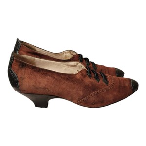 May include: Brown suede lace-up shoes with black trim and a low heel.