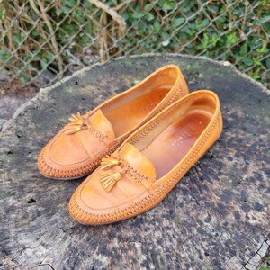 May include: A pair of brown leather tassel loafers with a woven pattern. The loafers have a pointed toe and a tassel detail on the front.
