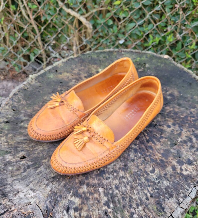 May include: A pair of brown leather tassel loafers with a woven pattern. The loafers have a pointed toe and a tassel detail on the front.