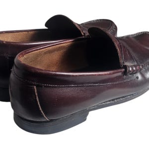 May include: A pair of brown leather loafers with a penny strap detail. The loafers have a slightly pointed toe and a low heel.