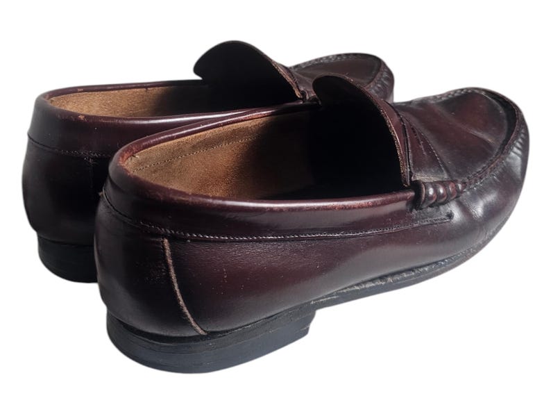 May include: A pair of brown leather loafers with a penny strap detail. The loafers have a slightly pointed toe and a low heel.
