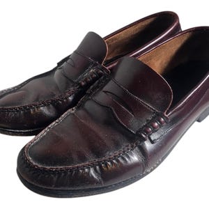 May include: A pair of dark brown leather loafers with a penny strap detail. The loafers have a classic design and are made of high-quality leather.