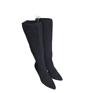 May include: A pair of black over-the-knee socks. The socks are made of a textured knit fabric and have a pointed toe. They are held together by a metal clip at the top.