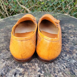 May include: A pair of brown leather loafers with tassels. The loafers have a woven pattern on the upper and a leather sole.