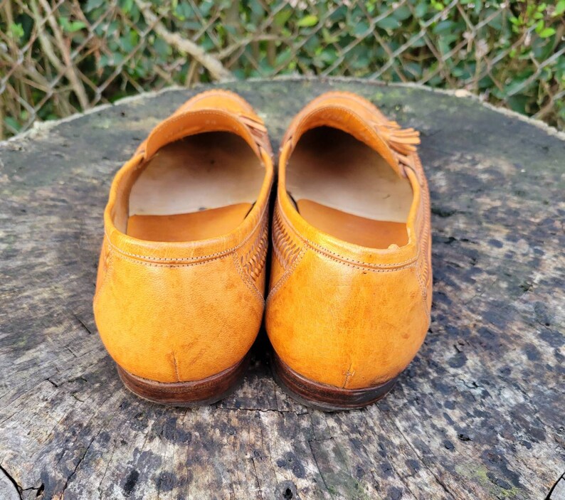 May include: A pair of brown leather loafers with tassels. The loafers have a woven pattern on the upper and a leather sole.
