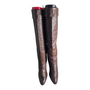 May include: A pair of brown leather knee-high boots with a pointed toe and a low heel.