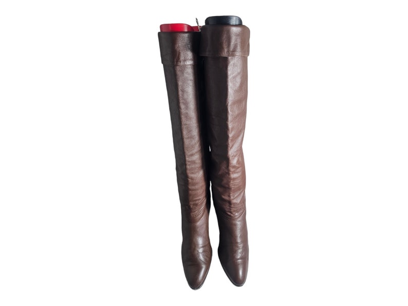 May include: A pair of brown leather knee-high boots with a pointed toe and a low heel.