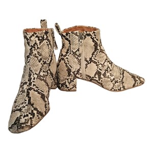 May include: A pair of beige ankle boots with a snakeskin pattern. The boots have a block heel and a zipper on the inside of each boot.