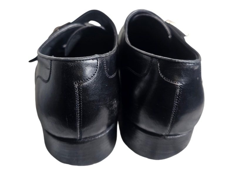 Pode incluir: Um par de sapatos de couro preto com fivelas. Os sapatos t&ecirc;m bico fino e salto baixo.