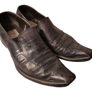 May include: A pair of black leather slip-on shoes with pointed toes and decorative stitching. The shoes have a slightly distressed look and feature a label with the text "Dylan Street All Rights Reserved".