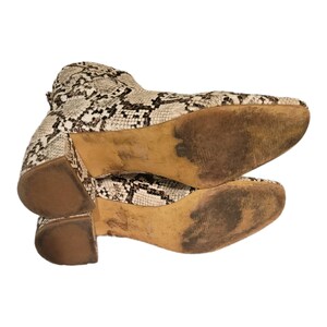 May include: A pair of brown and white snake print ankle boots with a block heel. The boots are stacked on top of each other, showing the soles.