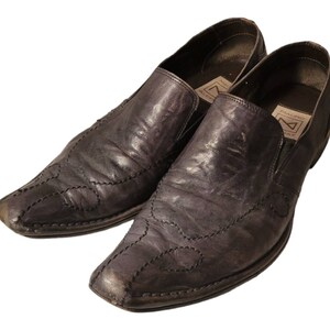 May include: A pair of black leather slip-on shoes with a pointed toe and decorative stitching. The shoes have a brand label on the inside of the shoe that reads "PREMIUM" and "MADE IN ITALY".
