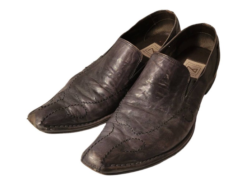 May include: A pair of black leather slip-on shoes with a pointed toe and decorative stitching. The shoes have a brand label on the inside of the shoe that reads "PREMIUM" and "MADE IN ITALY".