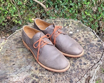 May include: A pair of brown leather lace-up shoes with orange laces. The shoes are sitting on a tree stump.