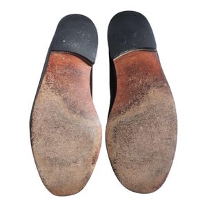 May include: A pair of brown leather shoe soles with a worn look. The soles are made of a textured material and have a slightly raised heel.
