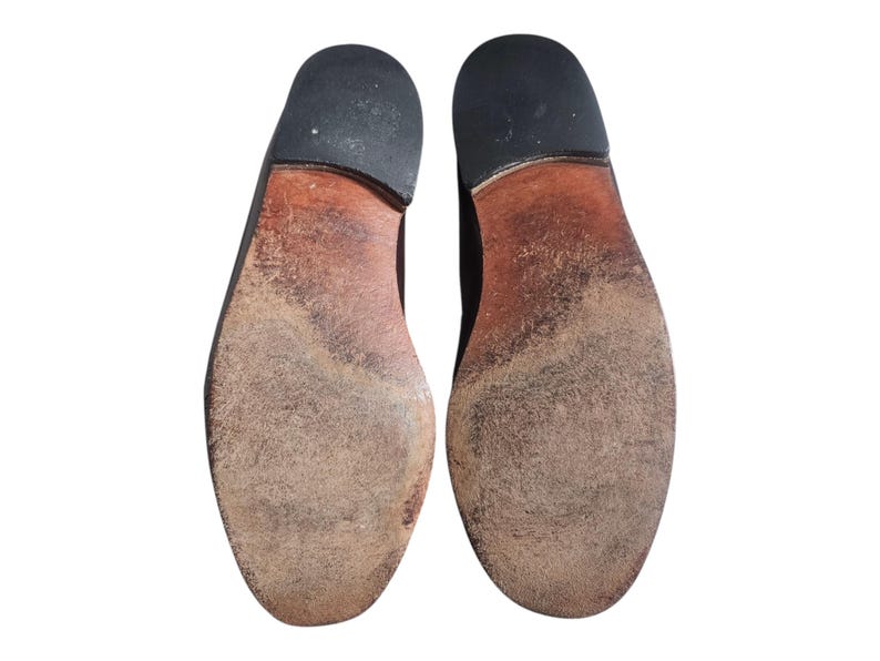 May include: A pair of brown leather shoe soles with a worn look. The soles are made of a textured material and have a slightly raised heel.