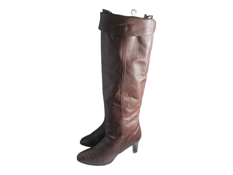 May include: Brown leather knee-high boots with a folded-over top and a low heel.