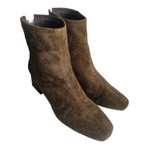 May include: A pair of brown suede ankle boots with a block heel. The boots have a pointed toe and a zipper on the inside of the ankle.