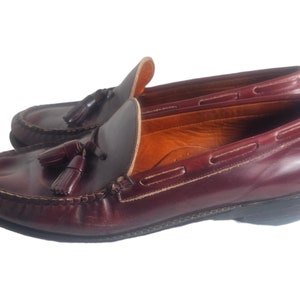 May include: A pair of burgundy leather tassel loafers with a brown leather sole. The loafers have a classic design and are perfect for casual or semi-formal occasions.